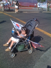 Girl in Stroller with Two Flags at Parade